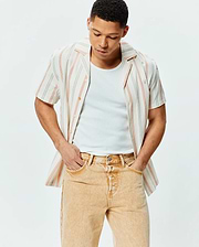 Mens Antoine Shirt, a relaxed fit off-white textured cotton short-sleeve button-up with thin blue and orange vertical stripes, featuring a small embroidered Psycho Bunny skull logo on the left chest.