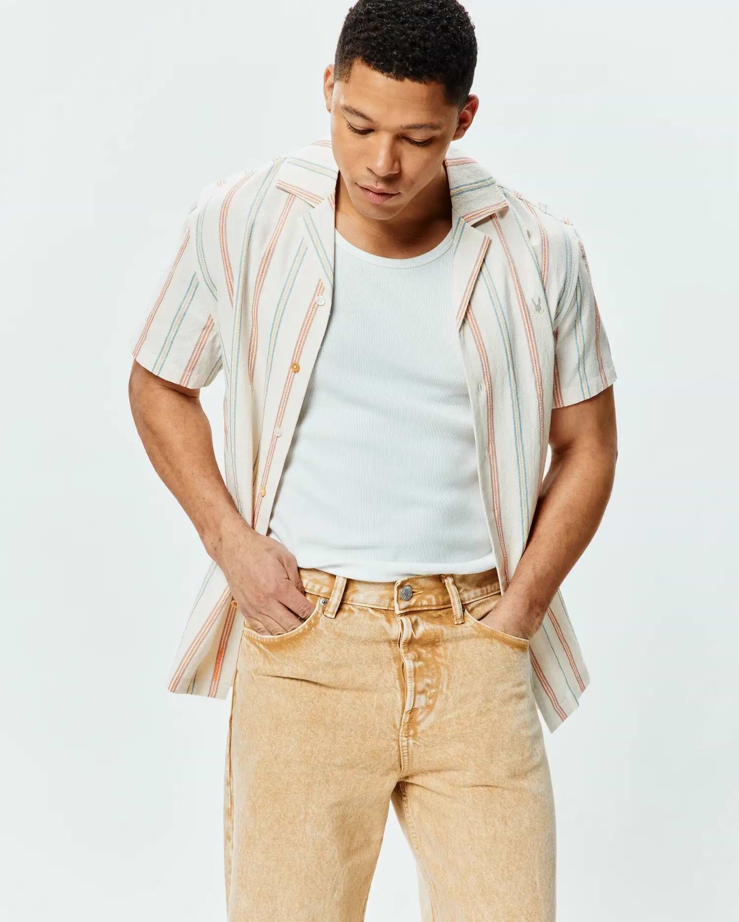 Mens Antoine Shirt, a relaxed fit off-white textured cotton short-sleeve button-up with thin blue and orange vertical stripes, featuring a small embroidered Psycho Bunny skull logo on the left chest.