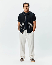 Mens Brad Linen Shirt, black, relaxed fit, short-sleeve with white embroidered palm trees, contrast stitching, and a small Psycho Bunny tag, paired with light beige relaxed linen pants.