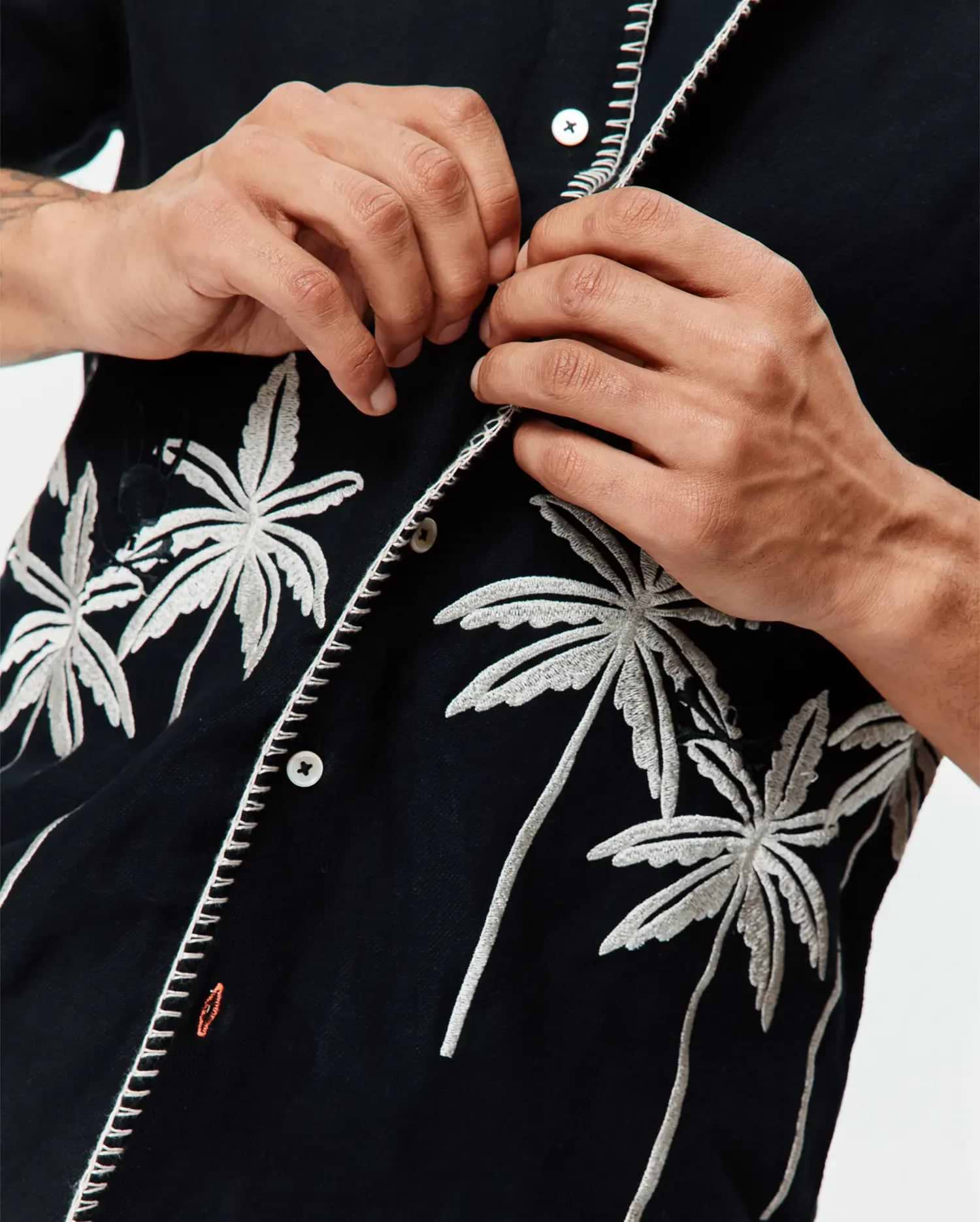 Mens Brad Linen Shirt, black with white embroidered palm trees, white contrast stitching on the placket, and a small orange Psycho Bunny logo on the chest.