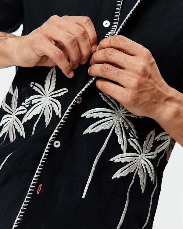 Mens Brad Linen Shirt, black with white embroidered palm trees, white contrast stitching on the placket, and a small orange Psycho Bunny logo on the chest.