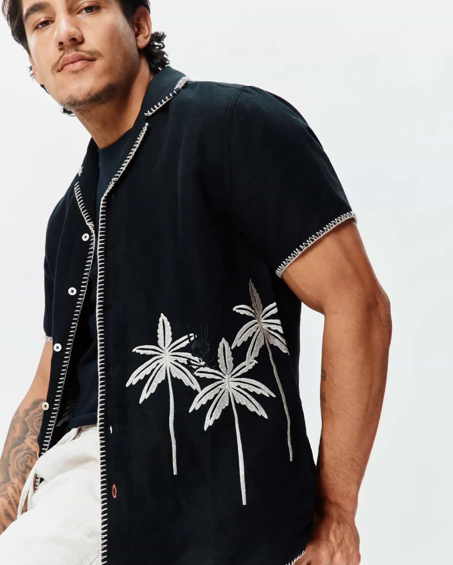 Mens Brad Linen Shirt, black, with prominent white zigzag stitching. Features embroidered silver palm trees and a small black Psycho Bunny skull logo on the chest. Relaxed fit.