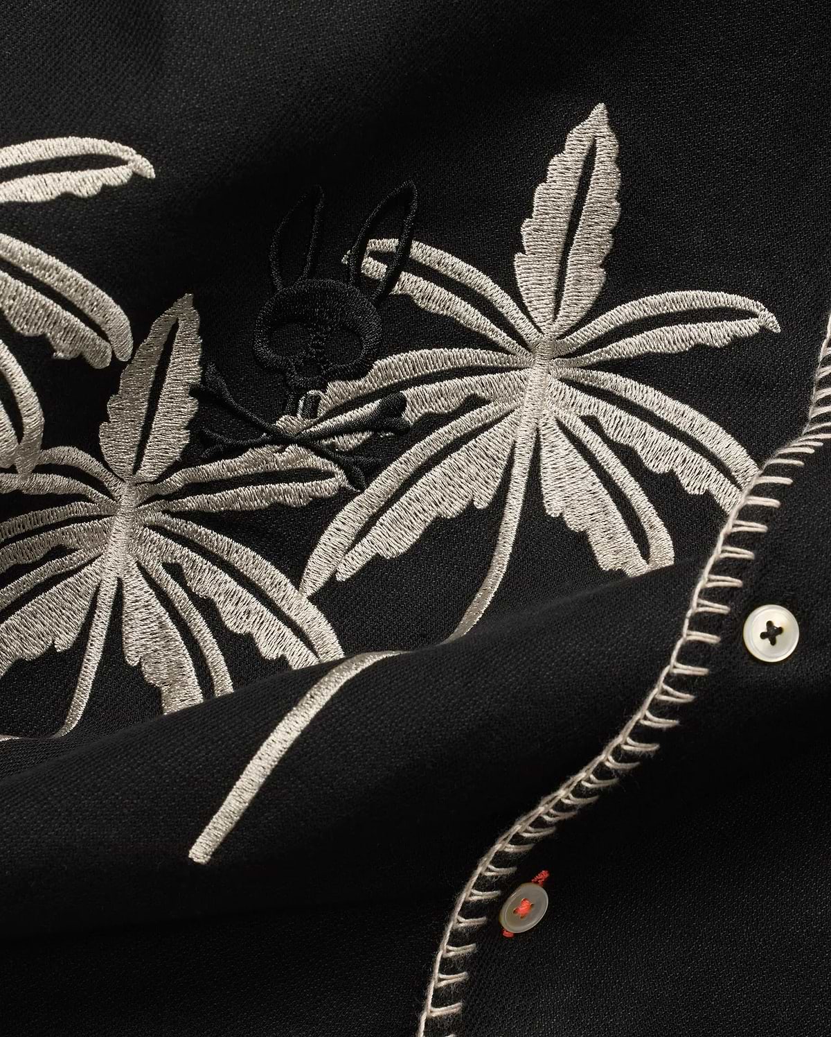 Mens Brad Linen Shirt in black, with beige embroidered palm leaves, a subtle black Psycho Bunny skull logo, white buttons with orange thread, and decorative white stitching.