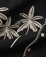 Mens Brad Linen Shirt in black, with beige embroidered palm leaves, a subtle black Psycho Bunny skull logo, white buttons with orange thread, and decorative white stitching.