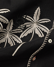 Mens Brad Linen Shirt in black, with beige embroidered palm leaves, a subtle black Psycho Bunny skull logo, white buttons with orange thread, and decorative white stitching.