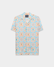 Mens Frank Tencel Shirt, a relaxed fit short-sleeve camp collar shirt in light blue, orange, and cream with an all-over tiled pattern featuring Psycho Bunny skull logos and floral designs.