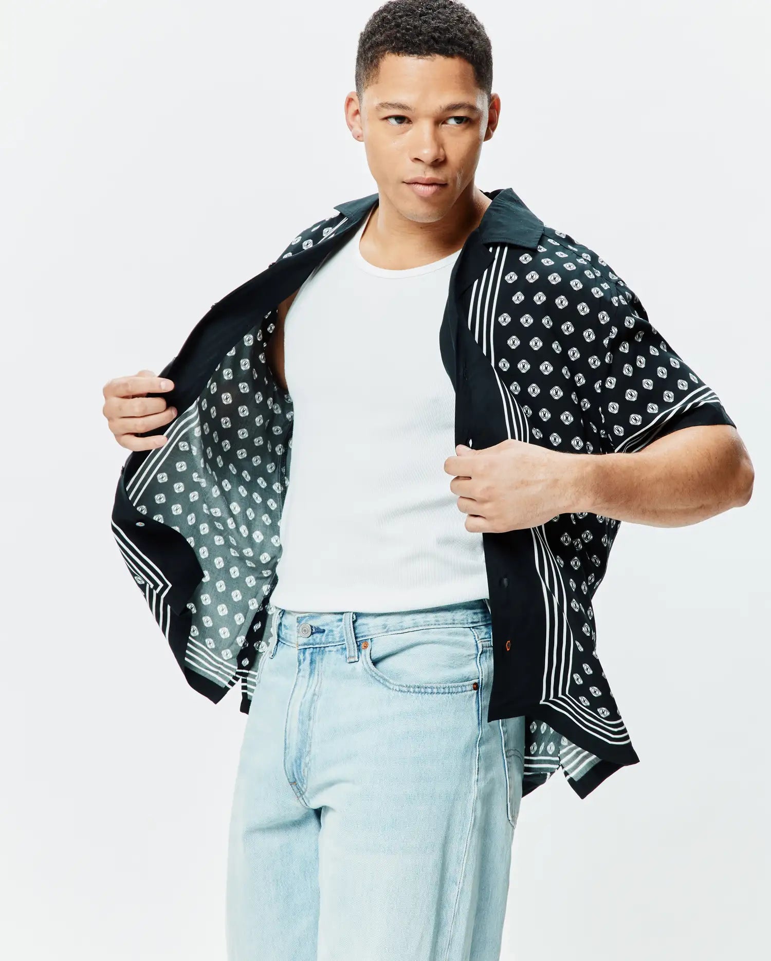 Mens Nick Tencel Shirt, a black short-sleeve button-up with a relaxed fit, featuring an all-over white Psycho Bunny skull logo pattern and vertical white stripes on the side panels.