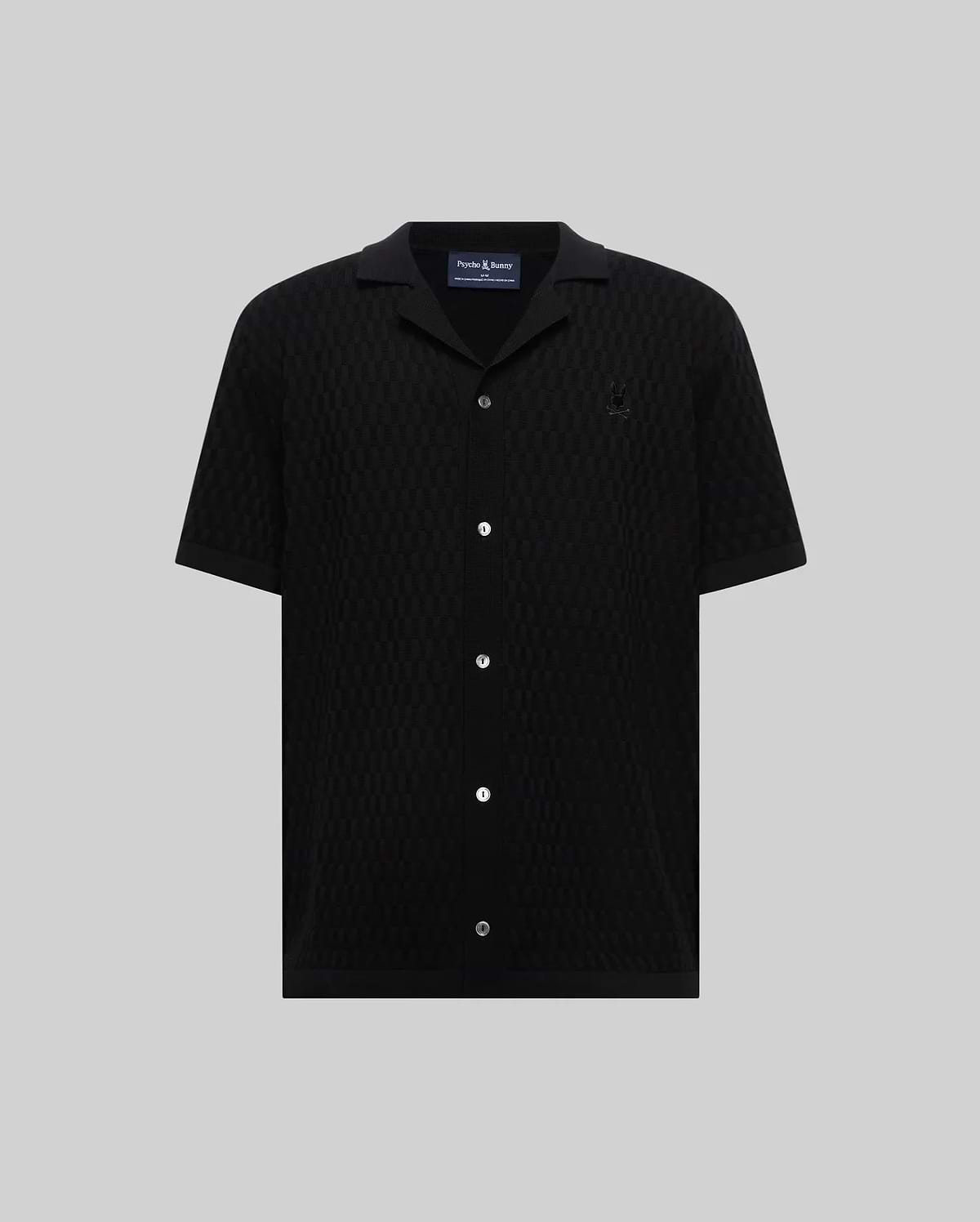 Mens Xandros Knit Shirt in black, featuring a classic fit, textured geometric knit fabric, a spread collar, full button-front with white buttons, and a small embroidered Psycho Bunny skull logo on the left chest.
