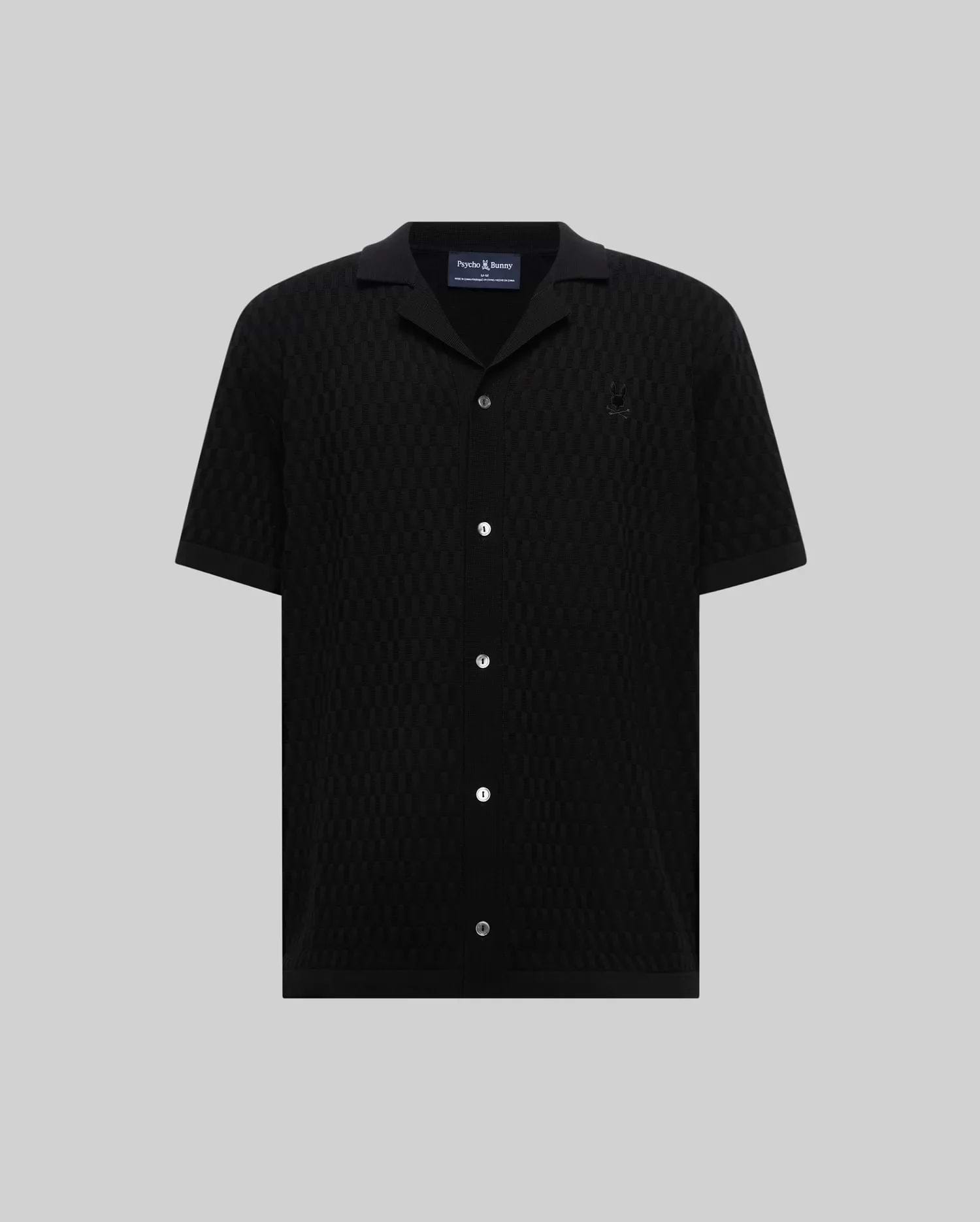 Mens Xandros Knit Shirt in black, featuring a classic fit, textured geometric knit fabric, a spread collar, full button-front with white buttons, and a small embroidered Psycho Bunny skull logo on the left chest.