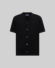 Mens Xandros Knit Shirt in black, featuring a classic fit, textured geometric knit fabric, a spread collar, full button-front with white buttons, and a small embroidered Psycho Bunny skull logo on the left chest.