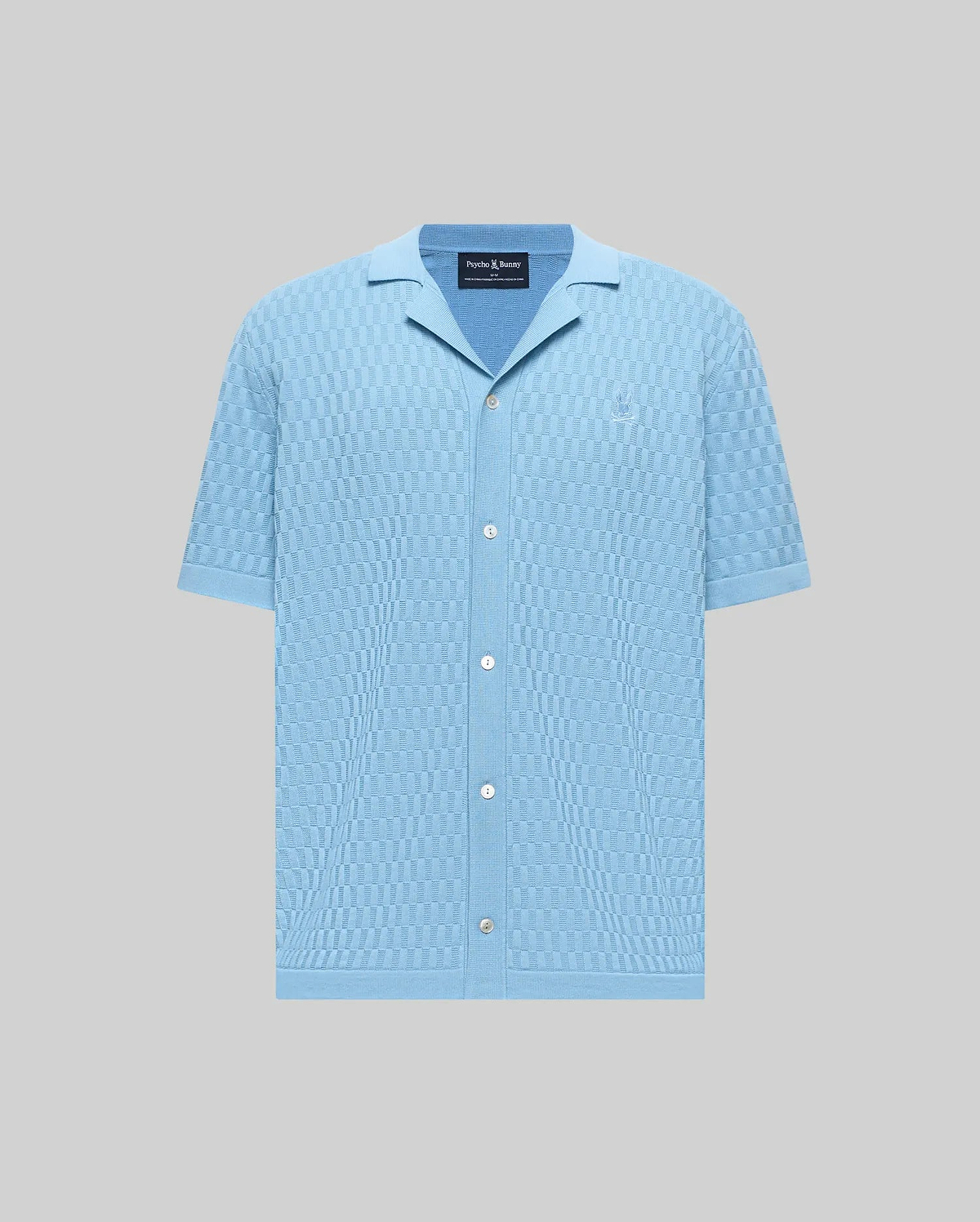 Mens Xandros Knit Shirt, a light blue relaxed fit full button-front shirt with a checkerboard knit pattern, spread collar, and small tone-on-tone embroidered Psycho Bunny skull logo on the left chest.