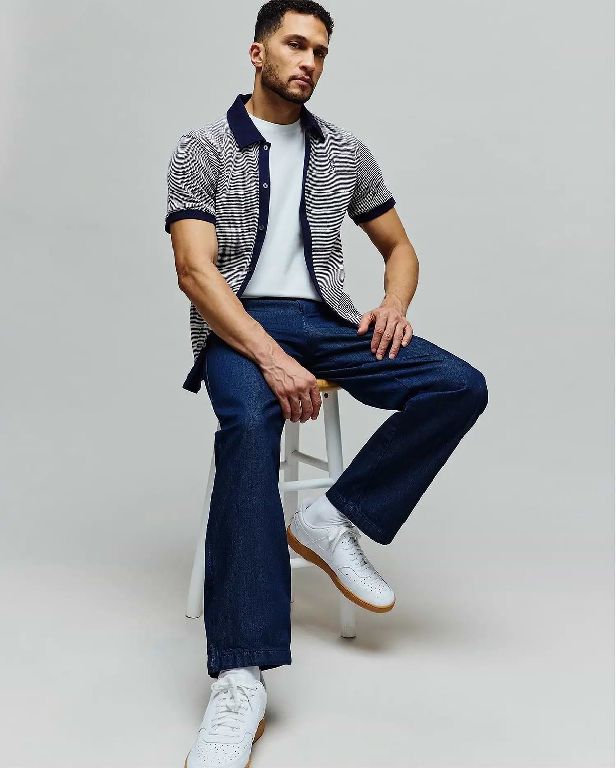 Mens Maxton Waffle Shirt, a classic fit white waffle knit short-sleeve shirt with navy collar and cuffs, featuring an embroidered Psycho Bunny skull logo on the chest, paired with a white tee and dark blue relaxed denim jeans.