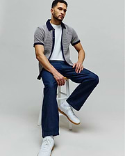 Mens Maxton Waffle Shirt, a classic fit white waffle knit short-sleeve shirt with navy collar and cuffs, featuring an embroidered Psycho Bunny skull logo on the chest, paired with a white tee and dark blue relaxed denim jeans.