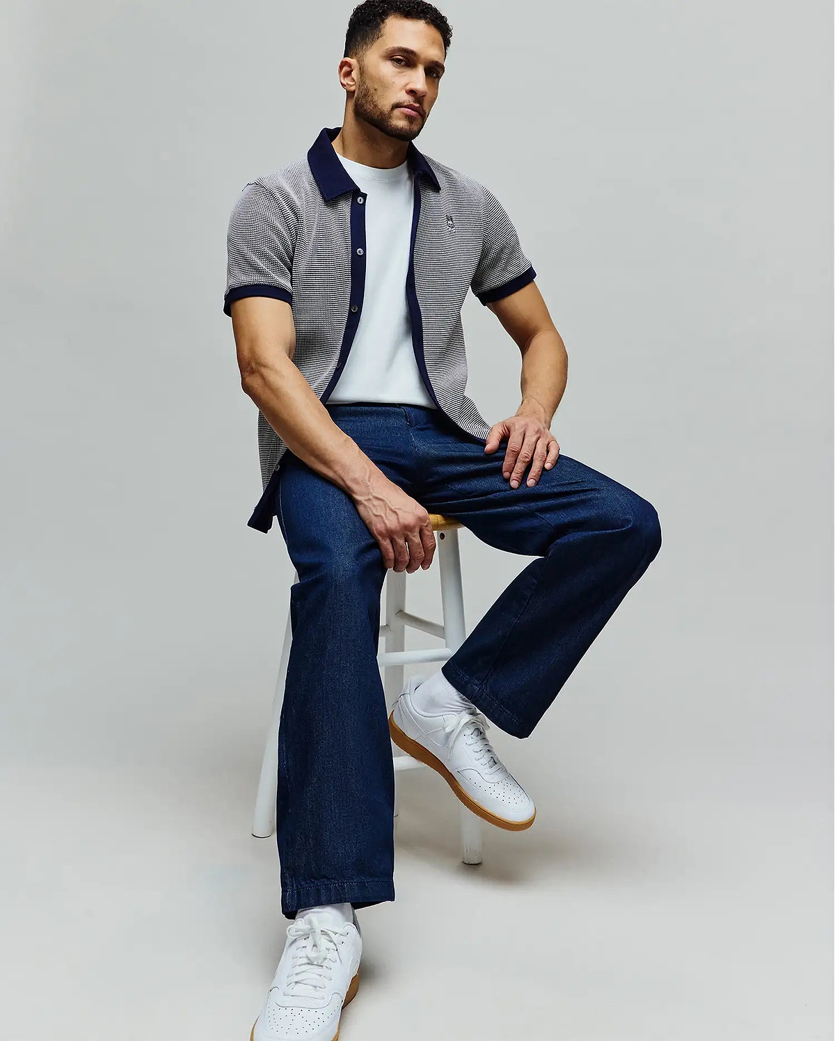 Mens Maxton Waffle Shirt, a classic fit white waffle knit short-sleeve shirt with navy collar and cuffs, featuring an embroidered Psycho Bunny skull logo on the chest, paired with a white tee and dark blue relaxed denim jeans.
