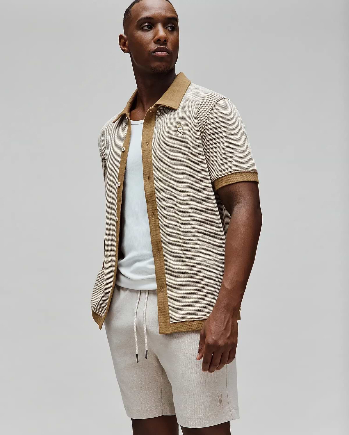 Mens Maxton Waffle Shirt, a relaxed fit short-sleeve collared shirt in a beige waffle knit with tan accents on the collar, placket, and cuffs, featuring a small embroidered Psycho Bunny skull logo on the left chest.