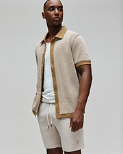 Mens Maxton Waffle Shirt, a relaxed fit short-sleeve collared shirt in a beige waffle knit with tan accents on the collar, placket, and cuffs, featuring a small embroidered Psycho Bunny skull logo on the left chest.