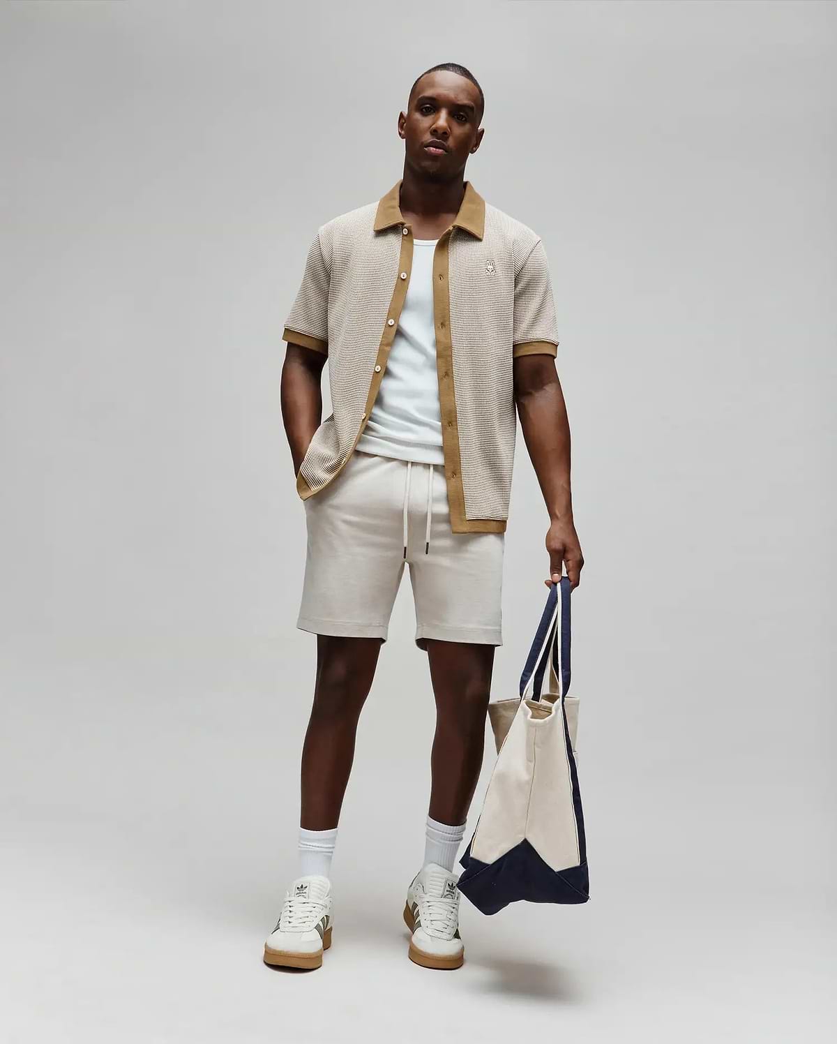 Mens Maxton Waffle Shirt, a relaxed fit beige waffle knit short-sleeve shirt with brown collar and placket, featuring a small embroidered Psycho Bunny logo on the left chest, paired with light beige drawstring shorts.