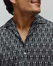 Mens Keon Tencel Shirt, a black relaxed fit camp collar shirt with smooth Tencel fabric, featuring an all-over white Psycho Bunny skull and crossbones logo pattern and white buttons.
