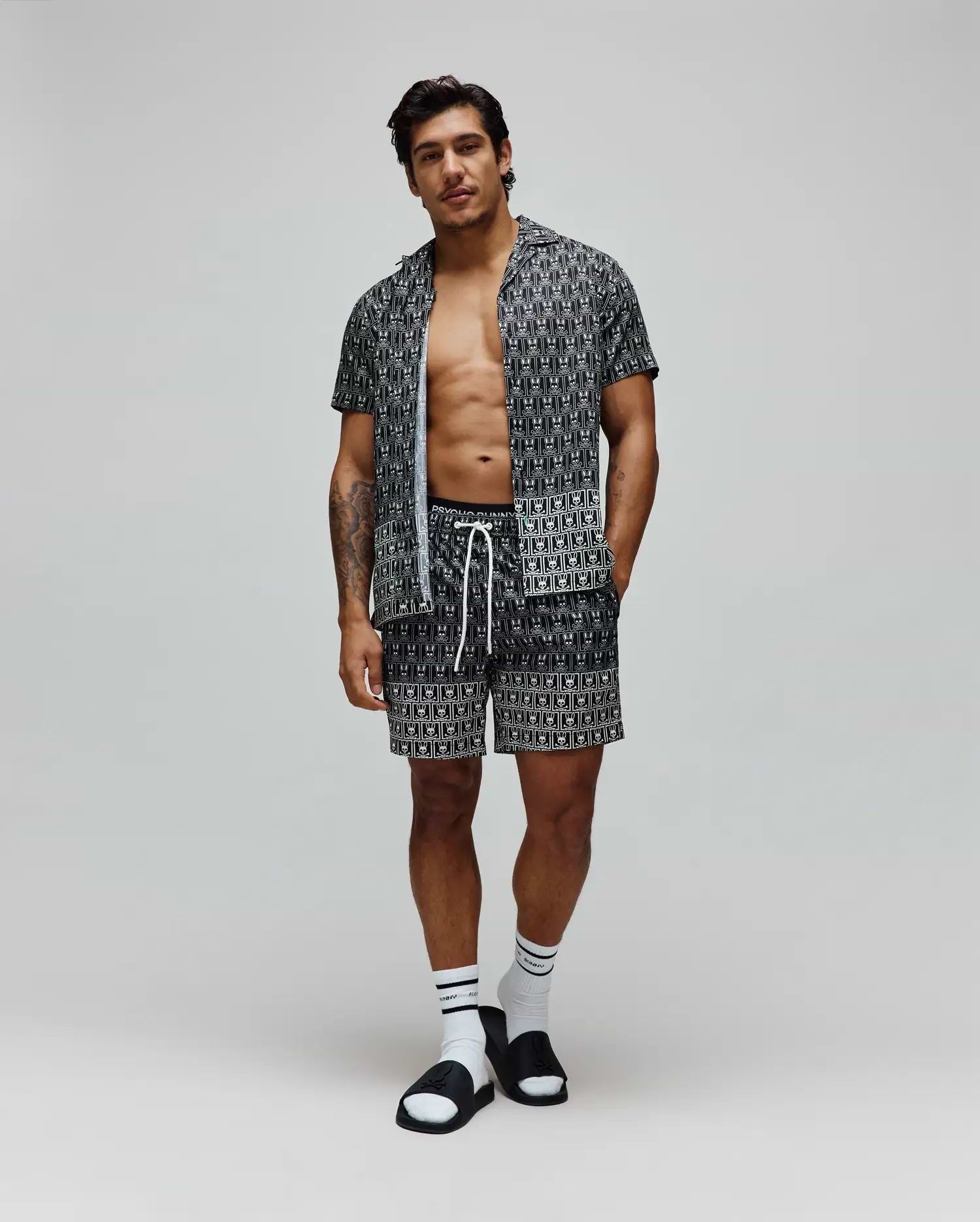 Black and white all-over Psycho Bunny skull logo pattern short-sleeve button-up shirt and matching shorts, both in a relaxed fit Tencel fabric with white drawstrings on the shorts. Mens Keon Tencel Shirt.