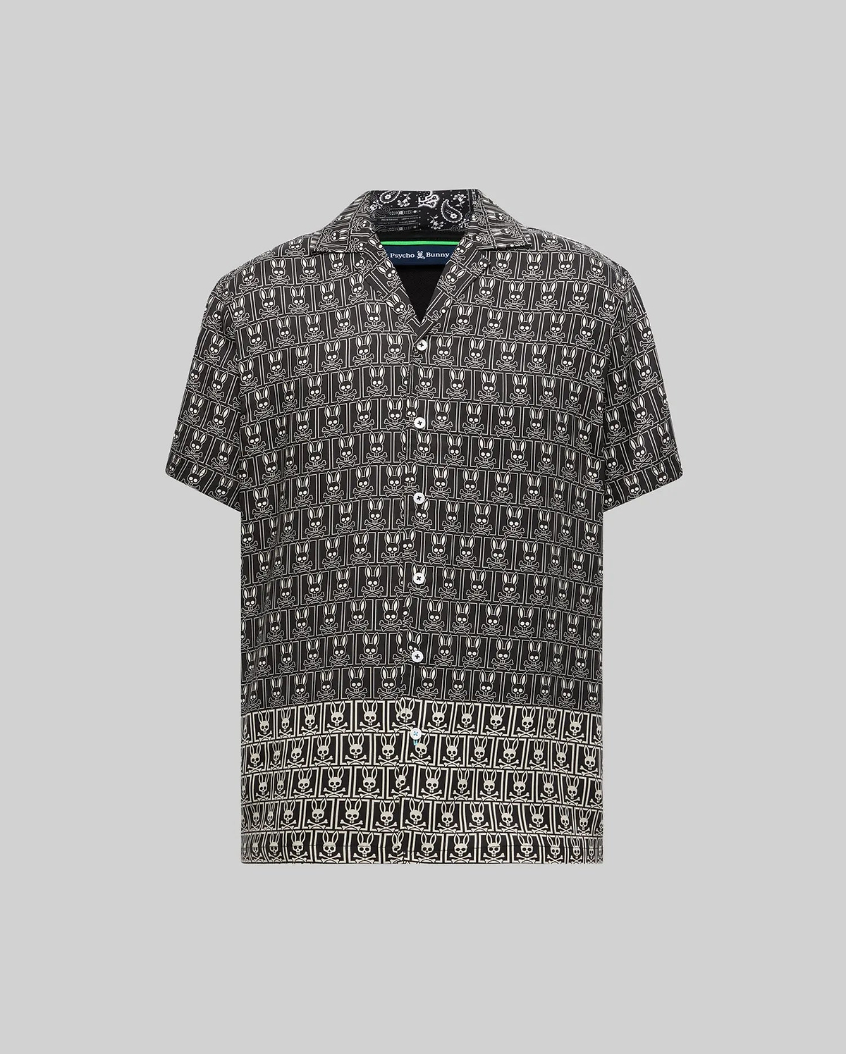 Mens Keon Tencel Shirt, a black short-sleeve button-up with a relaxed fit, featuring an all-over white Psycho Bunny skull logo pattern on smooth Tencel fabric, camp collar, and white buttons.