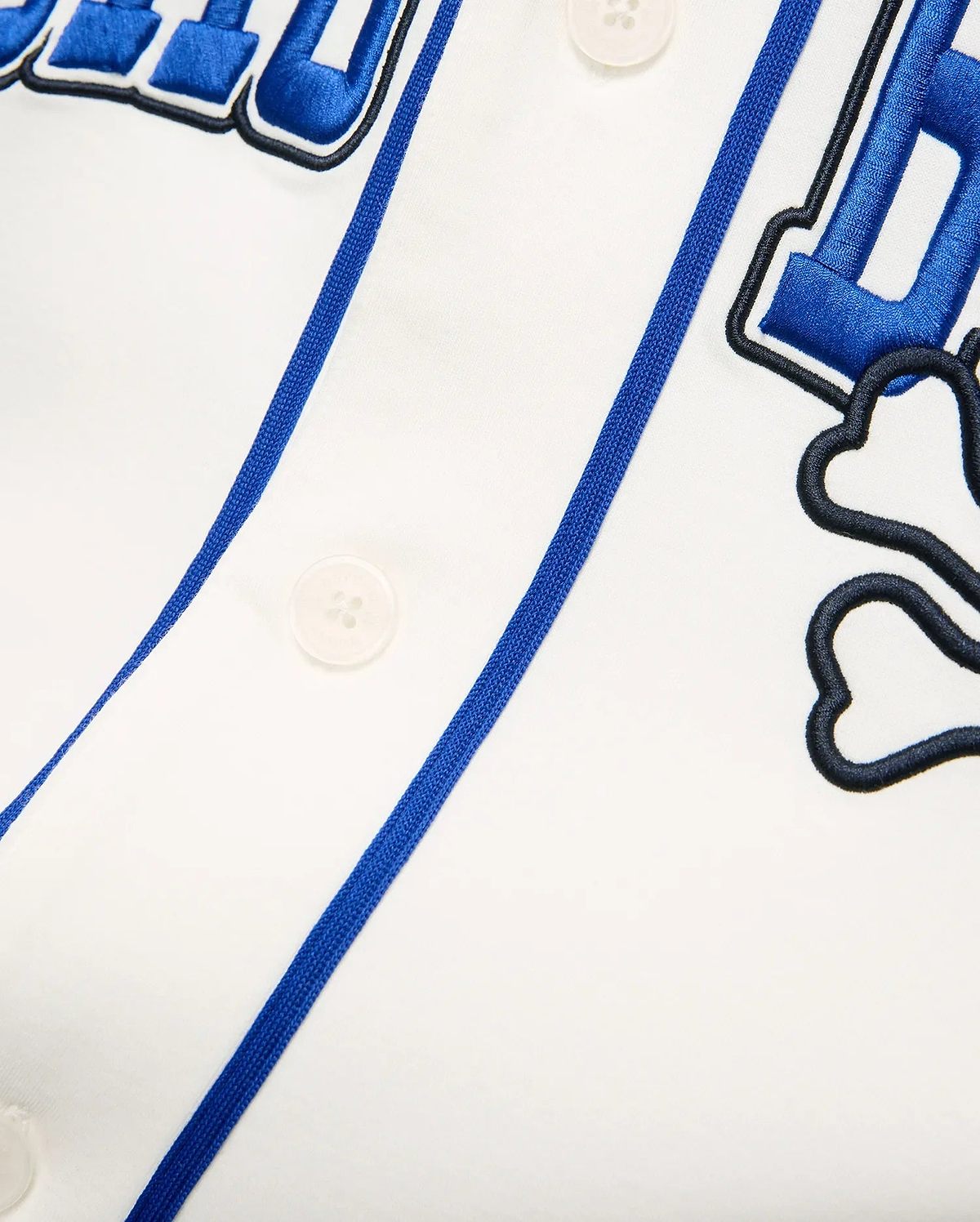 White Mens Nathaniel Baseball Shirt with blue piping, large embroidered blue text, and a black outlined Psycho Bunny skull logo on smooth jersey fabric.