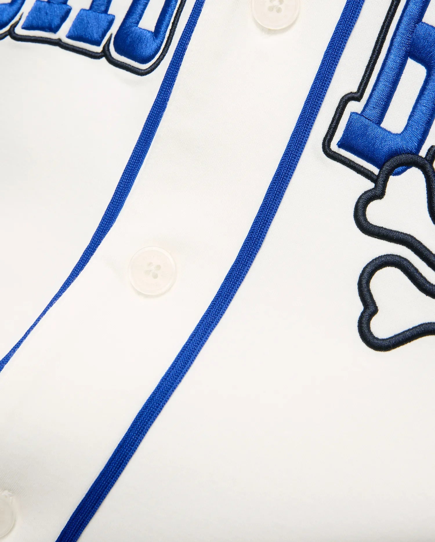 White Mens Nathaniel Baseball Shirt with blue piping, large embroidered blue text, and a black outlined Psycho Bunny skull logo on smooth jersey fabric.