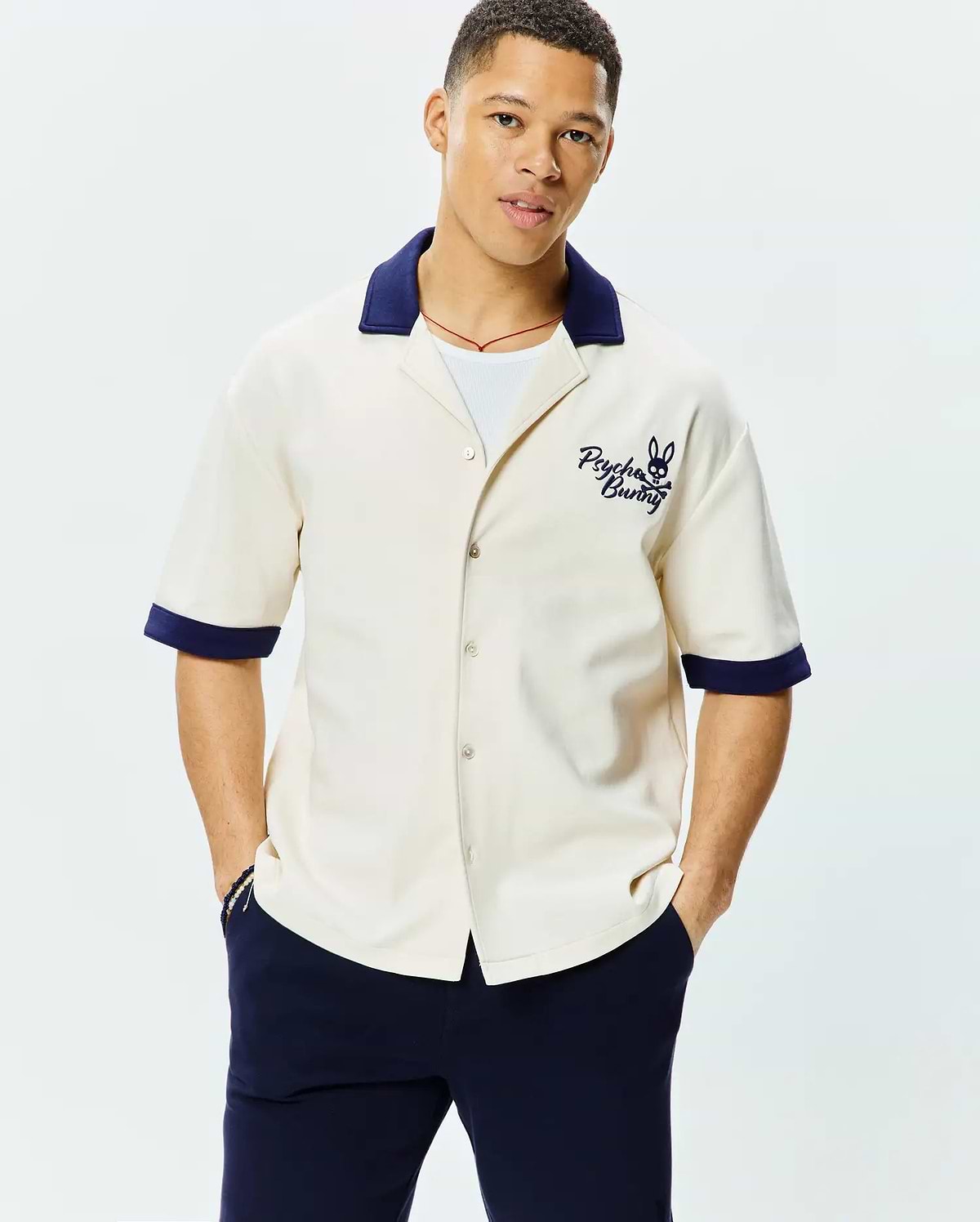 Mens Kelly Oversized Shirt in cream smooth knit, featuring a navy spread collar, matching banded cuffs, and a prominent embroidered Psycho Bunny skull logo with text on the left chest.