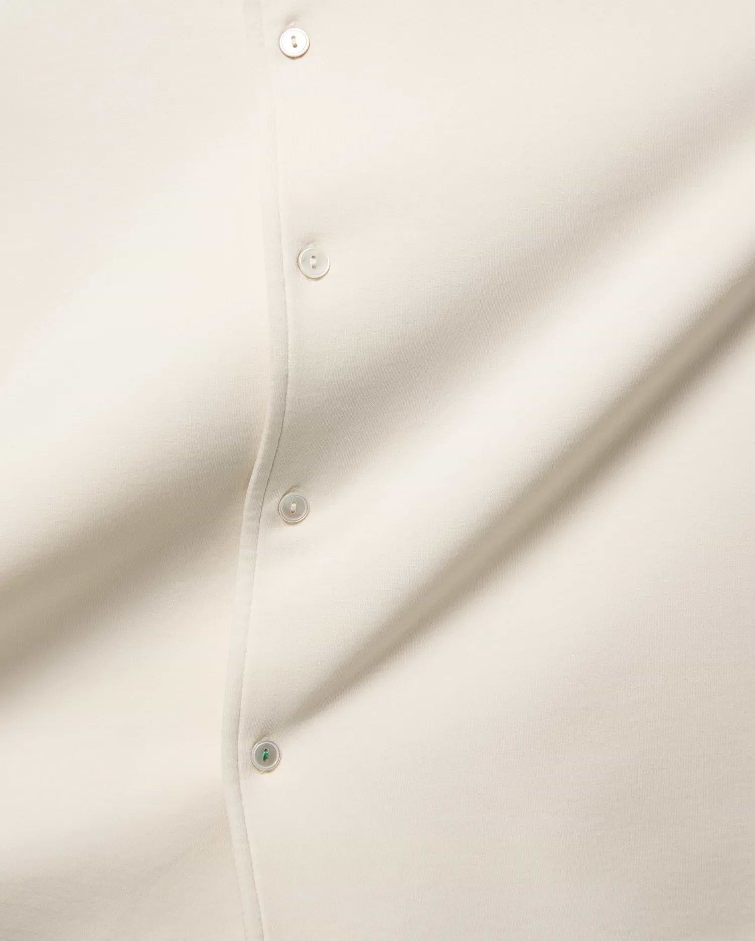 MENS KELLY OVERSIZED SHIRT in ecru, featuring a smooth jersey fabric, a button placket with cream buttons, and a distinctive green accent on the bottom button.
