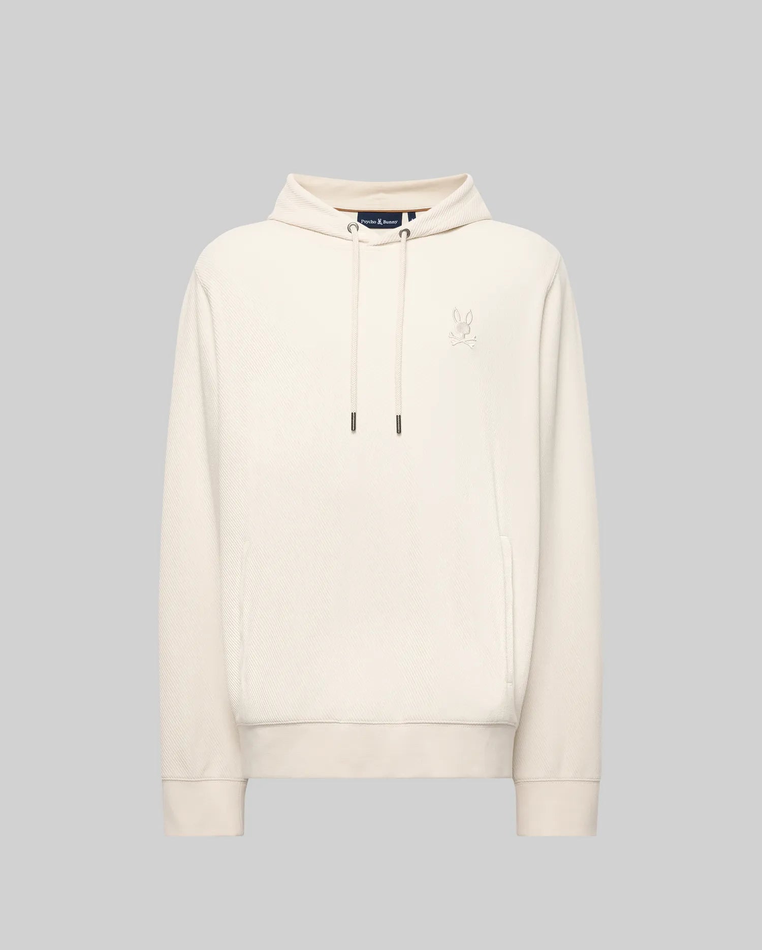 The MENS KAI TWILL TEXTURE HOODIE - MT0500019 by Psycho Bunny features a cream color, drawstrings, a small embroidered Bunny logo on the left chest, and ribbed cuffs and hem, shown against a light gray background.