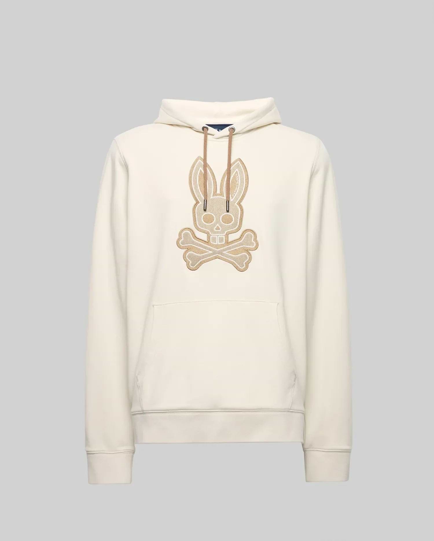 The Psycho Bunny MENS RYDER EMBROIDERED BUNNY PATCH HOODIE (MT0500029) is a cream-colored hoodie with a front pocket, drawstring hood, and large embroidered bunny skull and crossbones patch—ideal for cozy loungewear style.