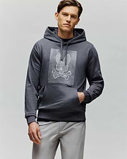 A man with short brown hair and a neutral expression models the Psycho Bunny MENS GRANT HOODIE (MT0500032), featuring a white, digital-inspired bunny and crossbones graphic, against a plain light gray background.