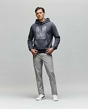 A man faces forward wearing the Psycho Bunny MENS GRANT HOODIE - MT0500032 with a digital-inspired graphic, paired with light gray pants and white sneakers, set against a plain light gray background.