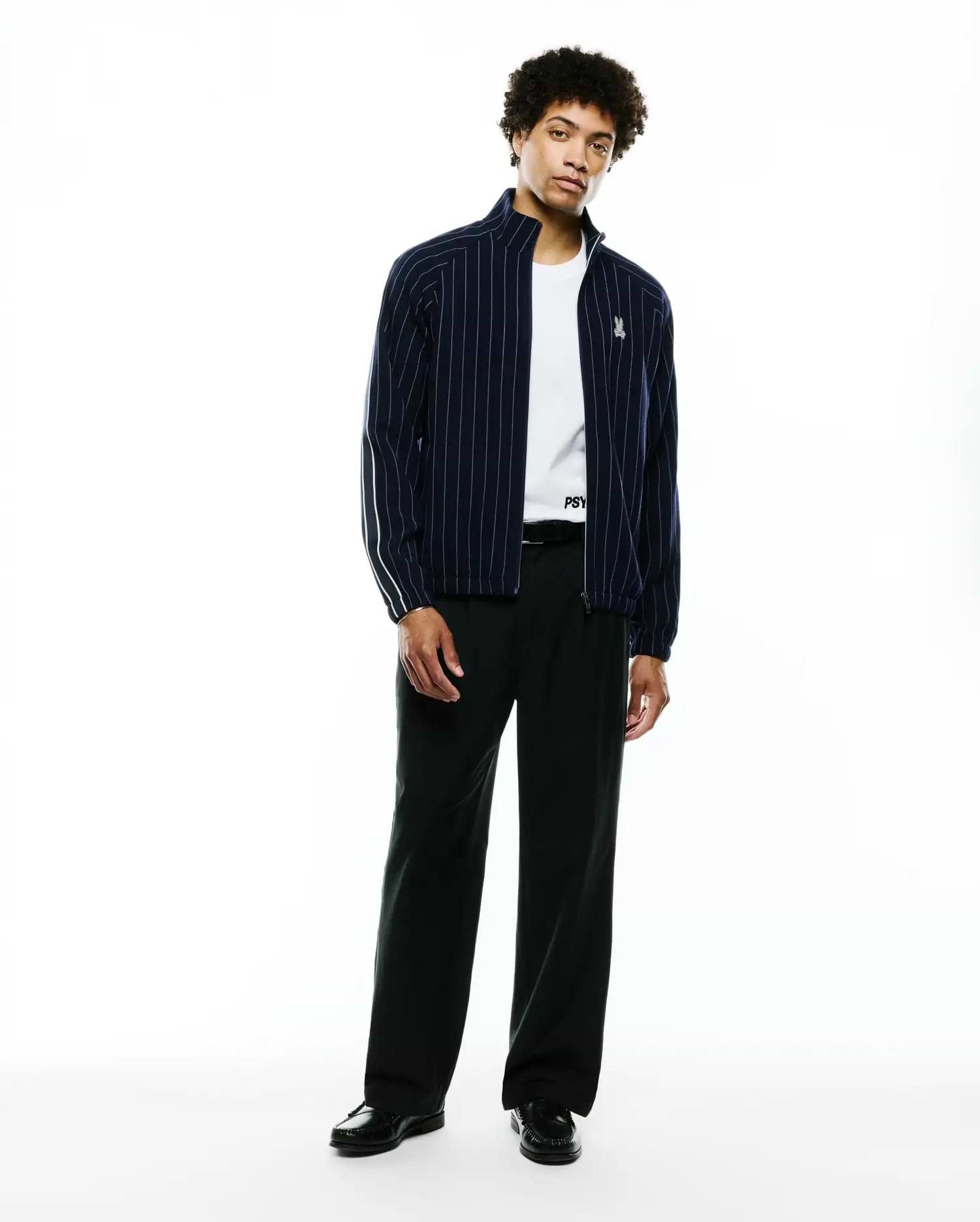 Mens Harland Double Weave Chalk Stripe Track Jacket in navy with white vertical pinstripes, a full zip, stand collar, and a small embroidered Psycho Bunny skull logo on the left chest, featuring white accent stripes on the sleeves. (5)