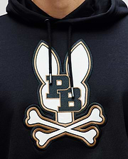 A close-up of the Psycho Bunny MENS WADE CORD PATCH HOODIE (MT0500112), a black premium cotton-blend hoodie featuring an embroidered logo with two bunny ears, bold "PB" initials, and crossed bones underneath.