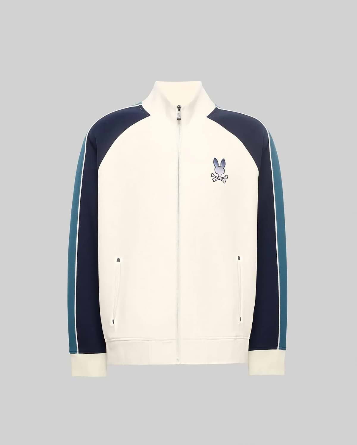 Cream full-zip track jacket with navy and teal color-block sleeves featuring a white stripe, classic fit, smooth knit, stand collar, and an embroidered Psycho Bunny skull logo on the left chest.