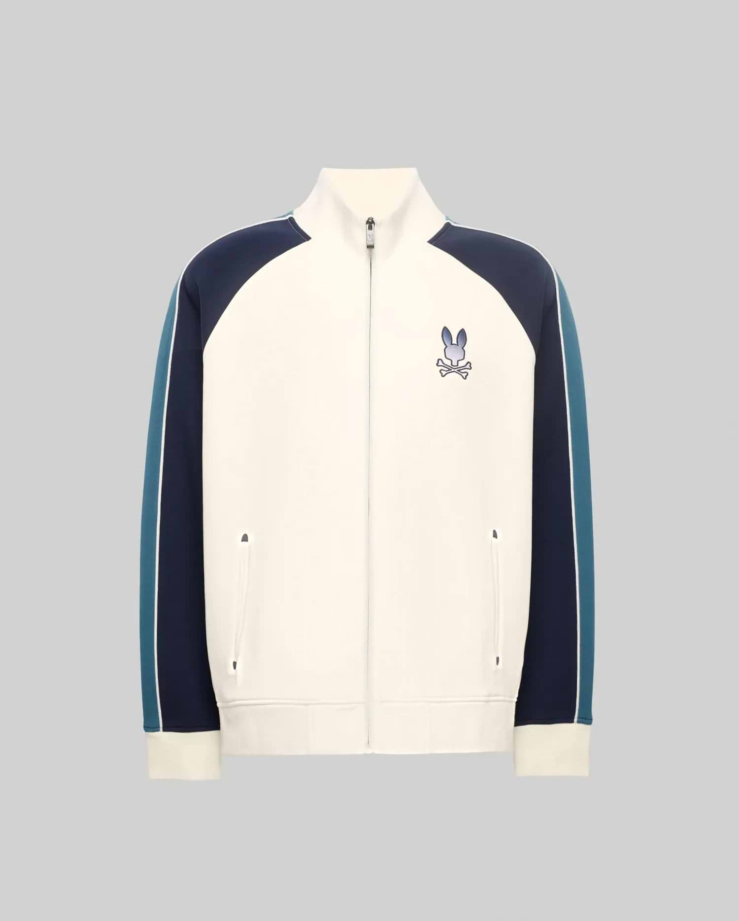 Cream full-zip track jacket with navy and teal color-block sleeves featuring a white stripe, classic fit, smooth knit, stand collar, and an embroidered Psycho Bunny skull logo on the left chest.