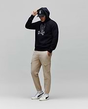 Mens Olivier Embroidered Hoodie: Relaxed fit navy French terry hoodie featuring a large white embroidered Psycho Bunny skull logo on the chest, complemented by beige cargo pants and a black logo cap.