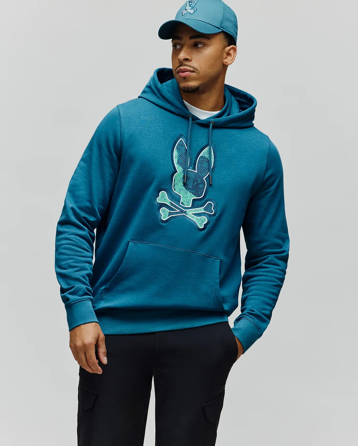 Mens Olivier Embroidered Hoodie, a classic fit teal blue heathered jersey hoodie featuring a large, central embroidered Psycho Bunny skull logo in light teal and green, with a drawstring hood and kangaroo pocket. (3)