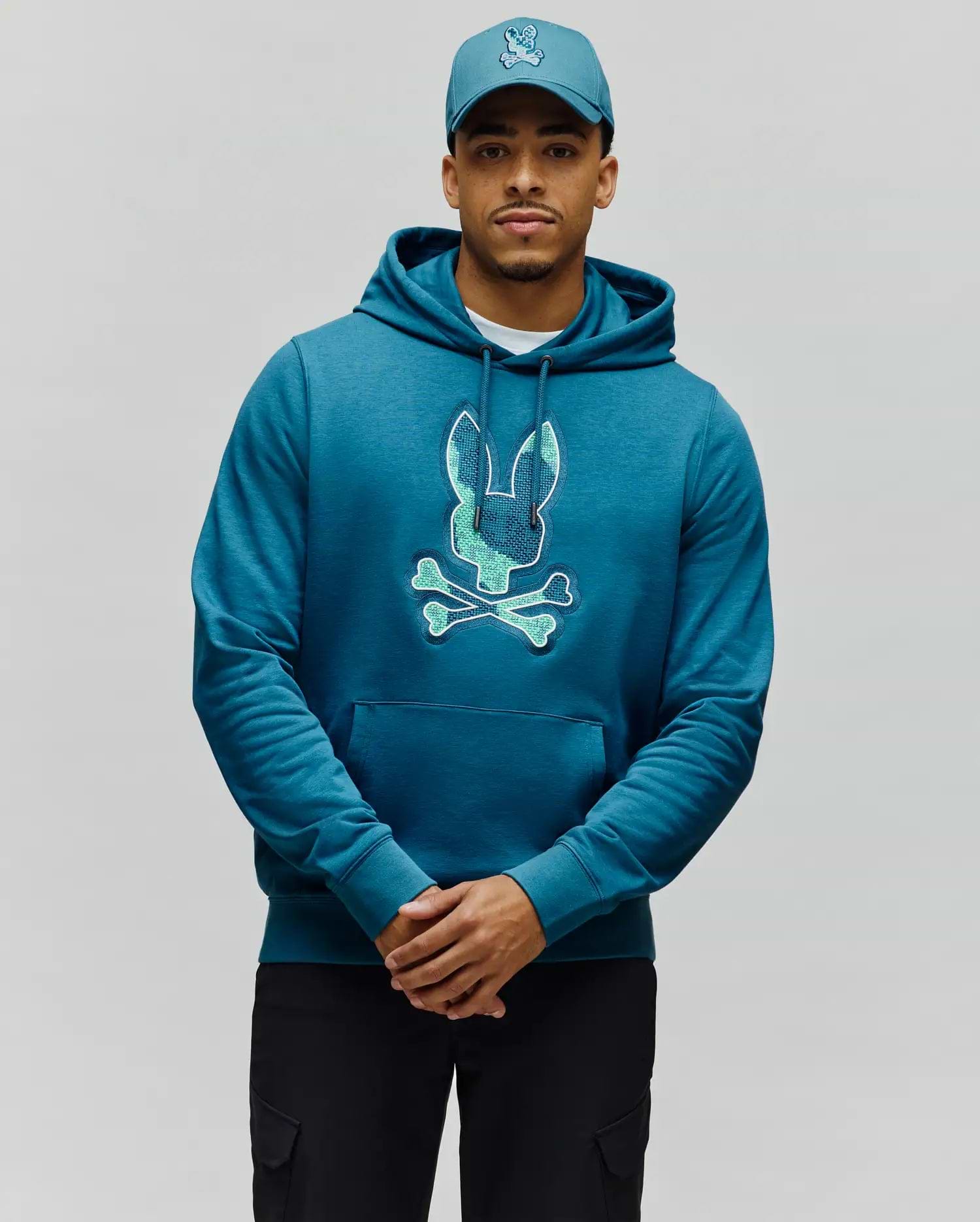 Mens Olivier Embroidered Hoodie in deep teal, featuring a large, central embroidered Psycho Bunny skull logo with a textured light blue-green fill and white outline, classic fit, soft heathered jersey fabric, and a kangaroo pocket. (1)