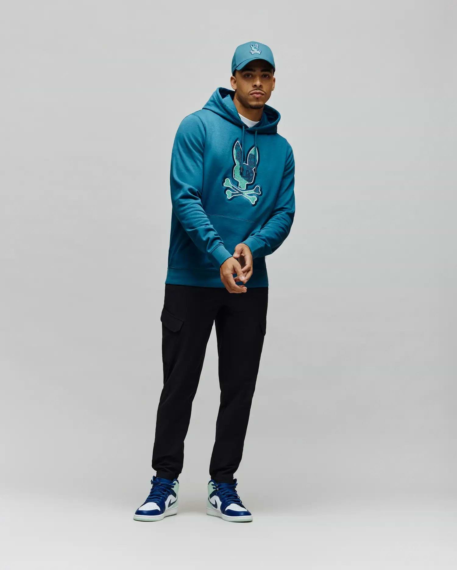 Mens Olivier Embroidered Hoodie, a classic fit deep teal french terry hoodie with a large, vibrant light teal embroidered Psycho Bunny skull logo on the center chest. (4)