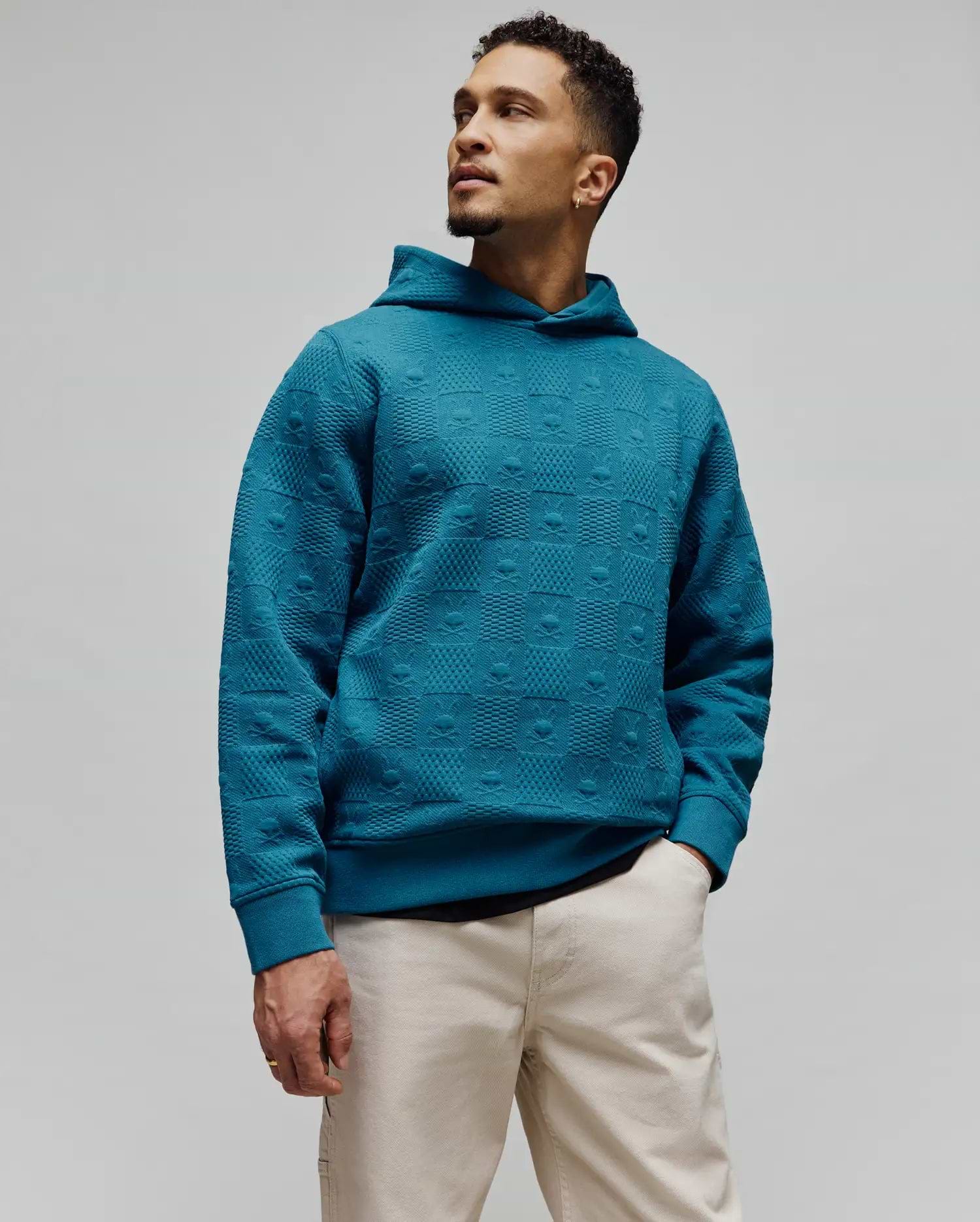 Mens Dustin Hoodie, a relaxed fit teal jacquard knit hoodie featuring an all-over embossed pattern of alternating Psycho Bunny skull logos and textured squares.