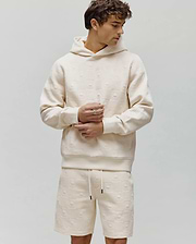 Mens Dustin Hoodie, a cream relaxed fit hoodie featuring an all-over embossed Psycho Bunny skull and crossbones logo pattern with a textured checkered design and a subtle orange neckline.