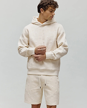 Mens Dustin Hoodie, a cream relaxed fit hoodie featuring an all-over embossed Psycho Bunny skull and crossbones logo pattern with a textured checkered design and a subtle orange neckline.