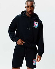 Soft black Mens Isaac Print Hoodie and matching shorts, featuring a relaxed fit. Both pieces showcase a large, vibrant, multi-color Psycho Bunny skull print with a distressed effect on the left chest and left leg.