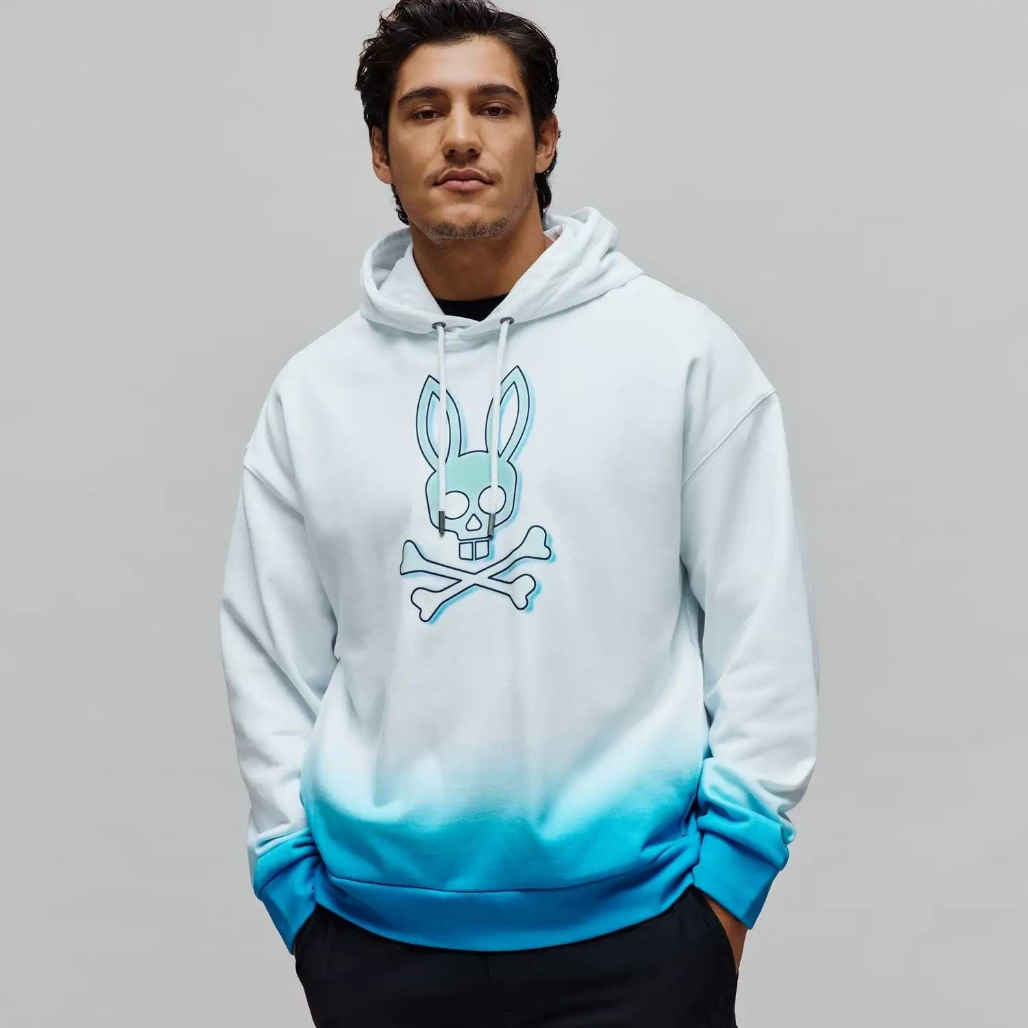 MENS DAX OVERSIZED HOODIE, a relaxed fit, smooth jersey hoodie featuring a white to vibrant blue ombre gradient and a large central teal Psycho Bunny skull and crossbones graphic. (1)