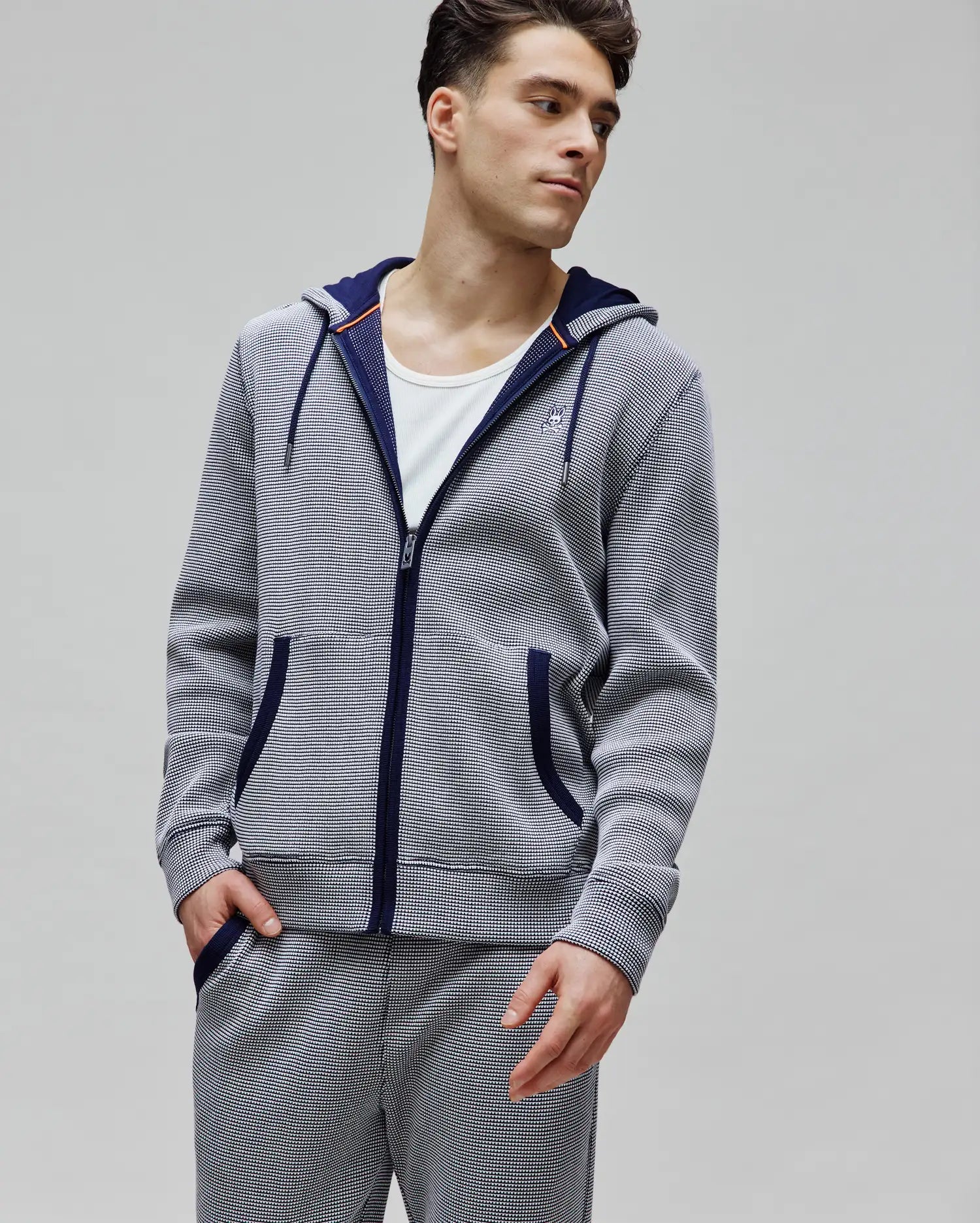 Mens Maxton Waffle Full Zip Hoodie in navy and white waffle knit, featuring a classic fit, full zip, drawstring hood with orange accents, front pockets, and a small embroidered Psycho Bunny skull logo on the left chest.