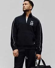 Mens Toby 1/4 Zip, a black relaxed-fit French terry pullover with white sleeve piping, a kangaroo pocket, and a prominent white Psycho Bunny skull logo on the left chest, plus a small lime green tag.