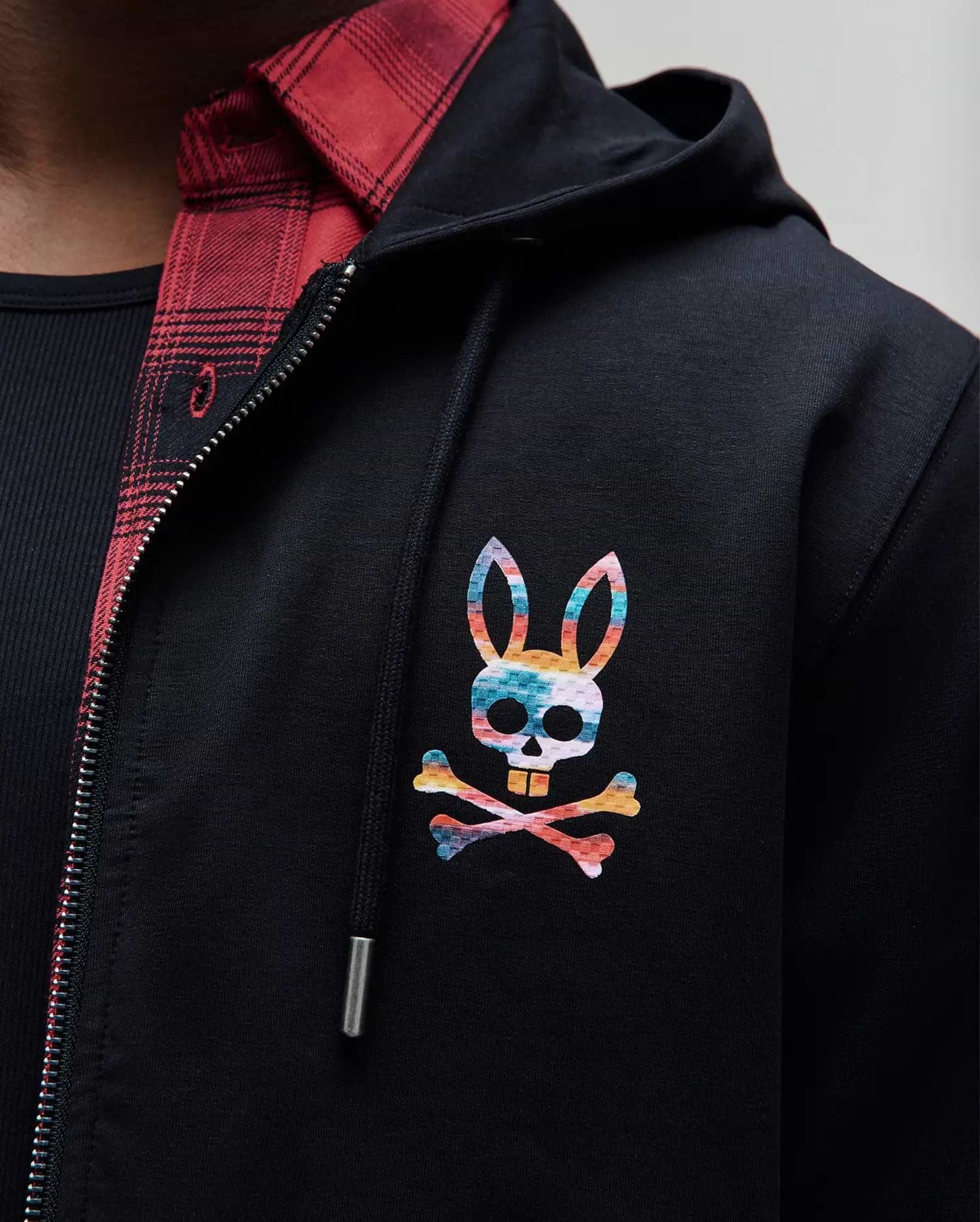 Black MENS RAPHAEL ZIP HOODIE in smooth jersey fabric, featuring a vibrant rainbow Psycho Bunny skull logo on the left chest, and a full silver zipper.