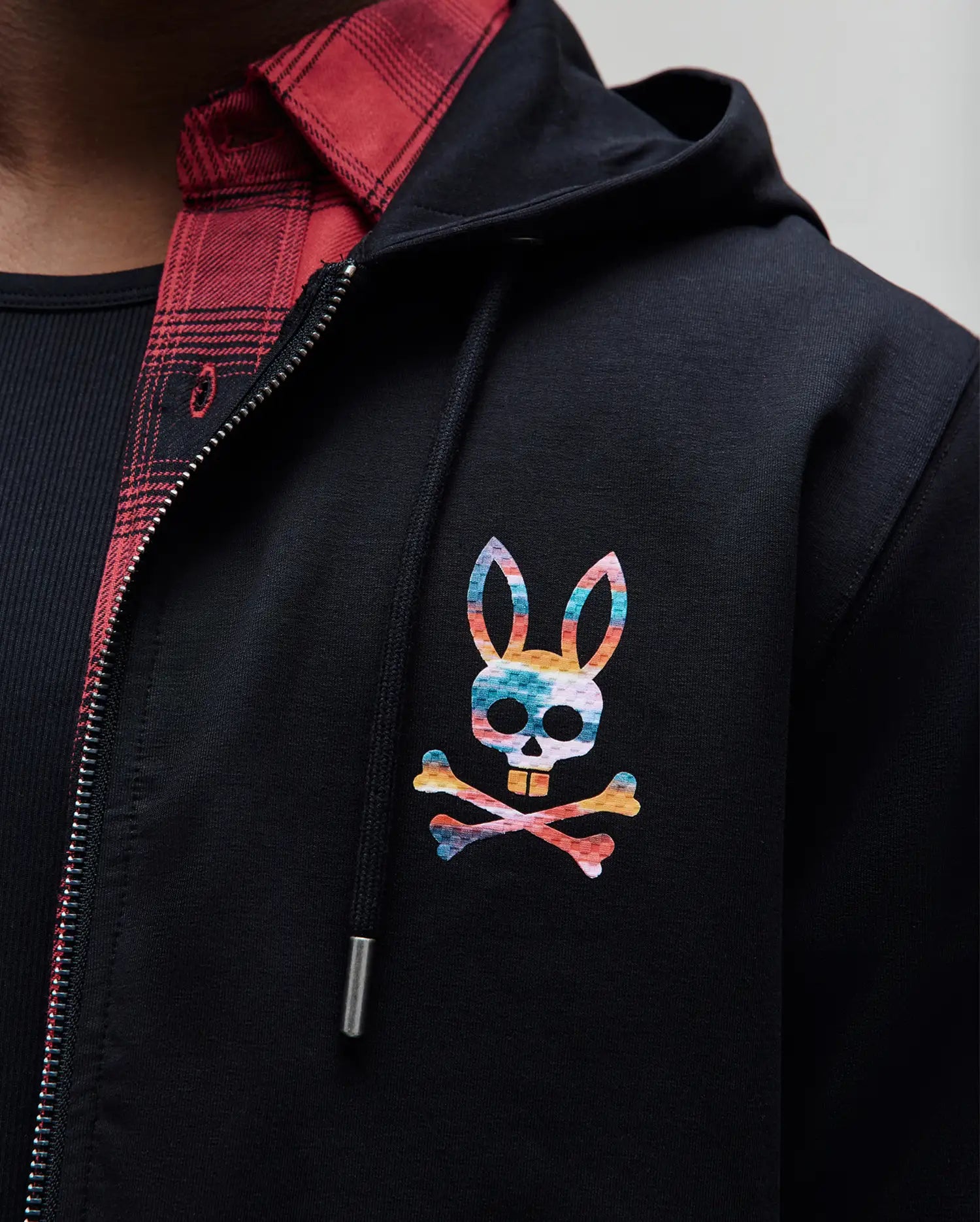 Black MENS RAPHAEL ZIP HOODIE in smooth jersey fabric, featuring a vibrant rainbow Psycho Bunny skull logo on the left chest, and a full silver zipper.