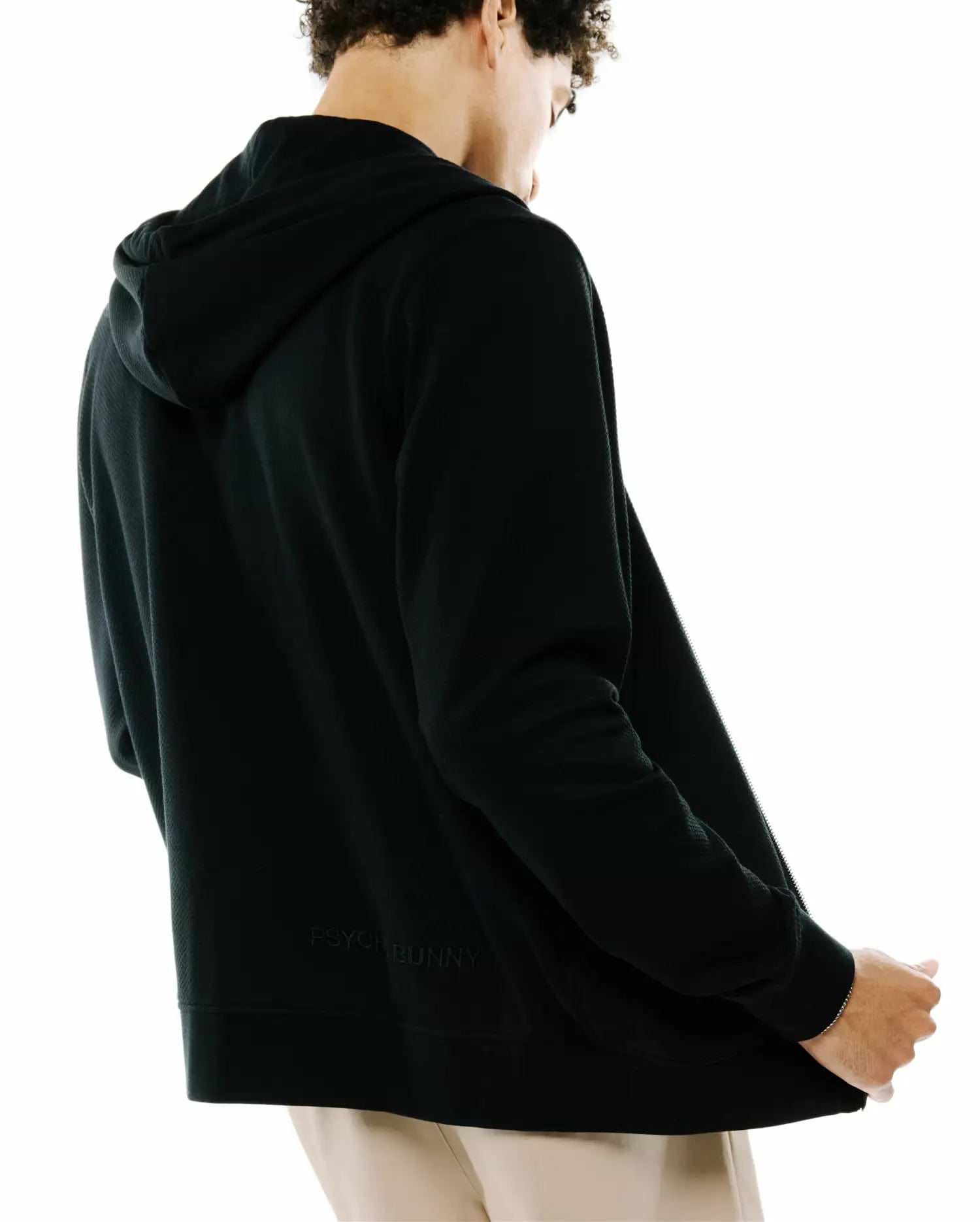 Mens Marc Textured Full Zip Hoodie in black, featuring a subtle textured fabric, full-zip closure, and a tone-on-tone embroidered PSYCHO BUNNY text logo on the lower back.